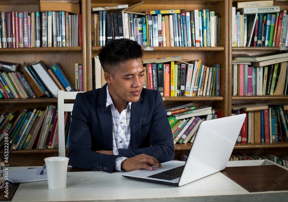 Young asian male student sitting in library with a laptop computer. Young asian male student sitting in library with a laptop computer.