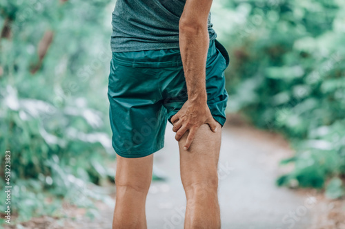 Leg muscle pain sports injury runner man touching painful hamstring muscle. Legs physiotherapy care athlete massaging sore muscles during running training in summer park outside. photo