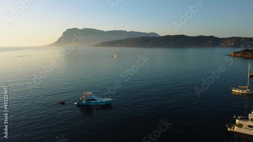 Flying over sailing boats on the tourist vacation island Sardinia in Italy at sunset at an idyllic sandy beach bay with clear blue turquoise and calm water close to Olbia. Aerial drone air view flight