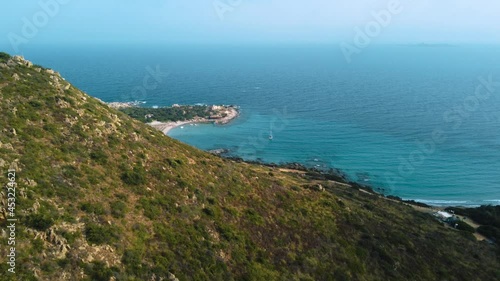 Sardinia clear blue turquoise and calm water at a natural sand beach coast bay in Italy with sun and sailing ship. Aerial drone air flight at a tourist holiday destination on nature vacation island.