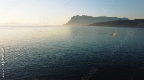 Sailing boat on the tourist vacation island Sardinia in Italy by sunset swimming in an idyllic sandy beach bay with clear blue turquoise and calm water close to Isola Tavolara and Olbia. Aerial drone