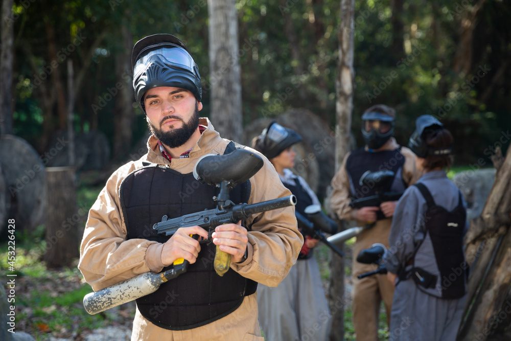 Fototapeta premium Man and his paintball sport team in protective uniform at paintball shooting range