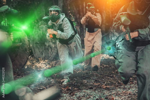 Excited male and female paintball players in protective uniform aiming and shooting with guns