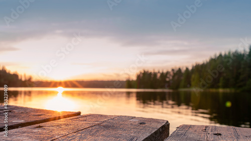 wood board table in front of sanset landscape of sparkling lake water. background is blurred.