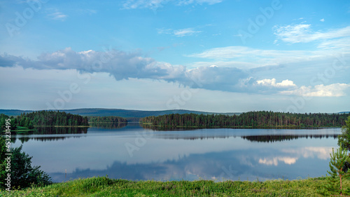 Summer lake near the forest. Blue sky and green grass.