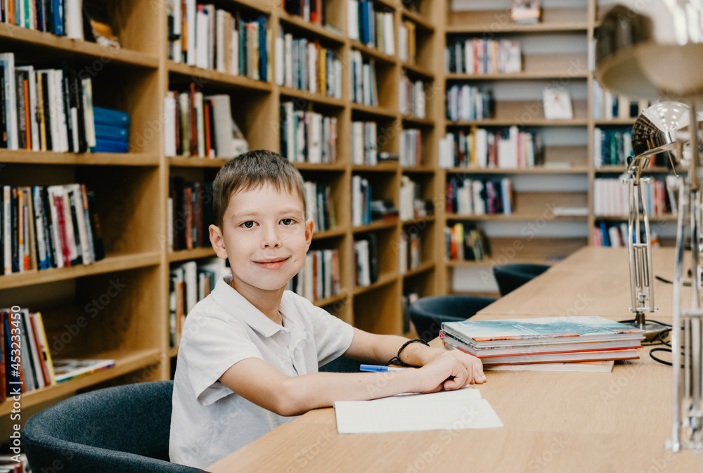The boy sits in the library and writes in a notebook at the table. Preparing for homework. a good student. Schoolboy loves to study. Free space at school. The boy sits in the library and writes in a notebook at the table. Preparing for homework. a good student. Schoolboy loves to study. Free space at school.
