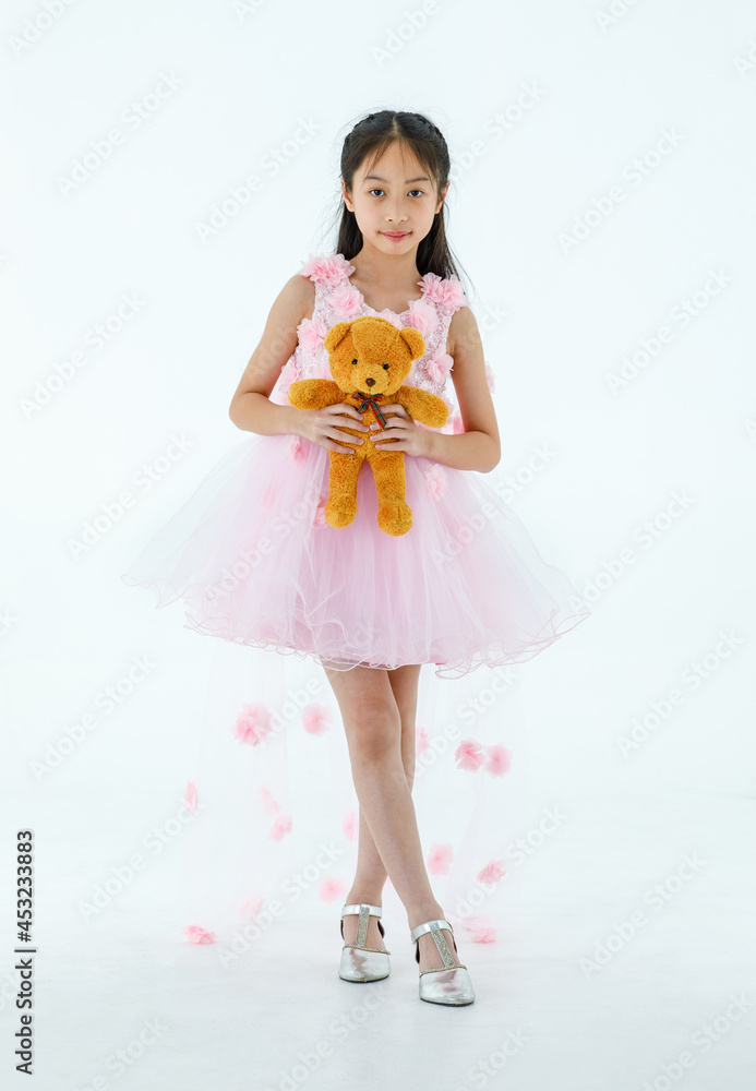 Portrait studio shot of Asian pretty girl wears white princess long rose flower dress fashion costume look at camera and hug fluffy orange teddy bear doll in front white background