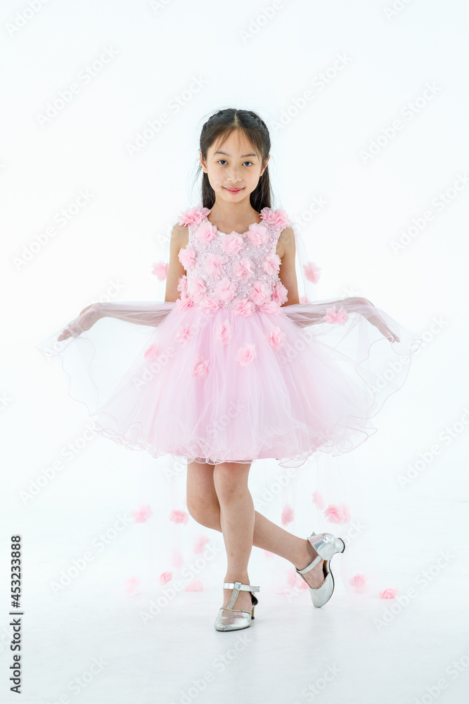 Naklejka premium Portrait isolated studio shot of little Asian cute ballerina kid in pink beautiful ballet dress with high heels standing smiling posing elegance gesture in front white background