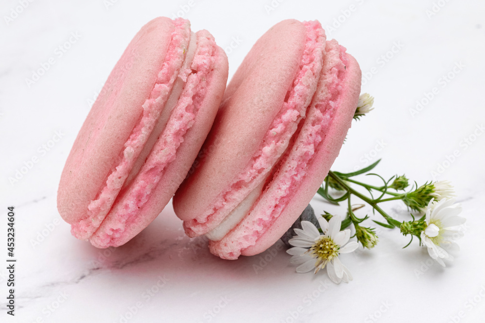 Close up of two pink macaroons or French macarons on a white marble top background.