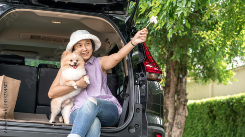  Asia women hugging her lovely puppy pomeranian dog at the back of suv car on travel tip and copy space