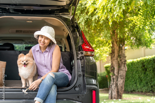  Asia women hugging her lovely puppy pomeranian dog at the back of suv car on travel tip and copy space