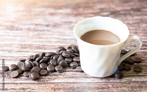 Portion of homemade hot cocoa in a cup with dark chocolate chips on a wooden background.