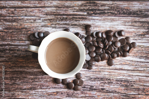 Portion of homemade hot cocoa in a cup with dark chocolate chips on a wooden background.