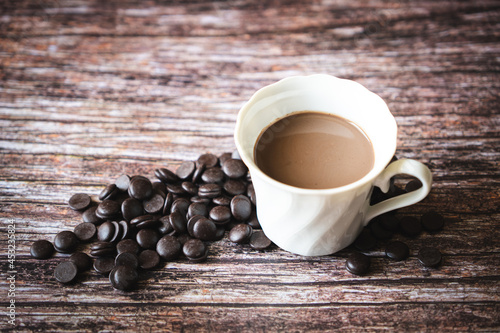 Portion of homemade hot cocoa in a cup with dark chocolate chips on a wooden background.