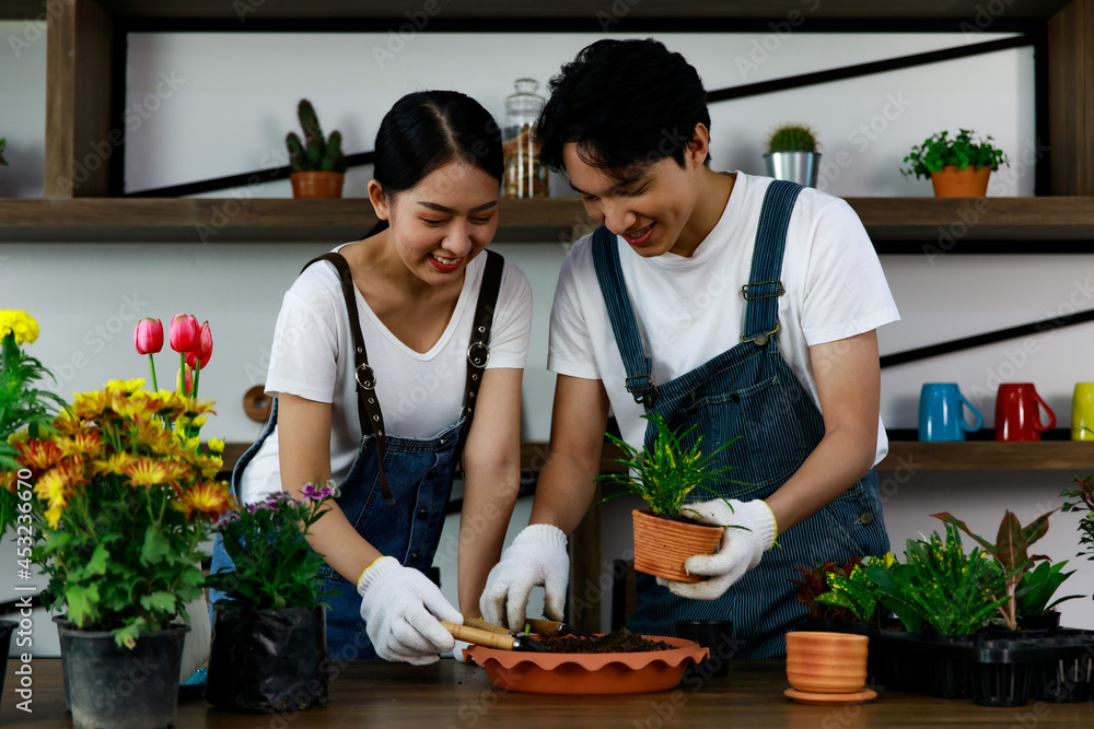 Young asian couple wearing jean overall and white t-shirt doing gardening and growing small plants and trees. Concept home garden hobby Young asian couple wearing jean overall and white t-shirt doing gardening and growing small plants and trees. Concept home garden hobby