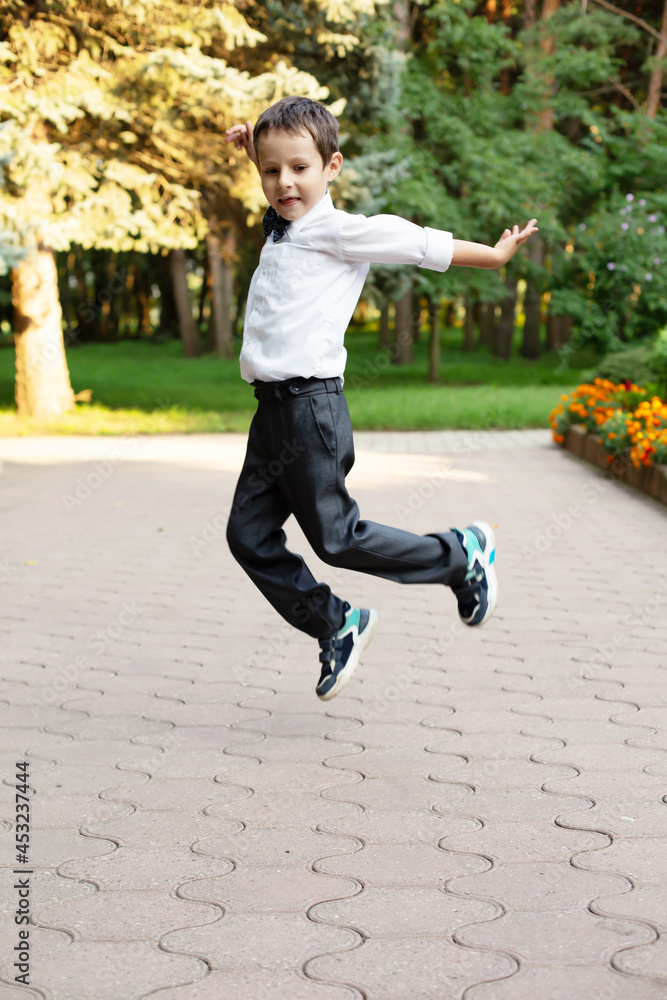 a beautiful little boy in a white shirt and gray trousers a schoolboy with a bow on his neck holds jumps