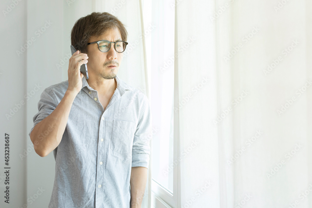 Asian businessman texting on smartphone standing next to window. Asian businessman texting on smartphone standing next to window.