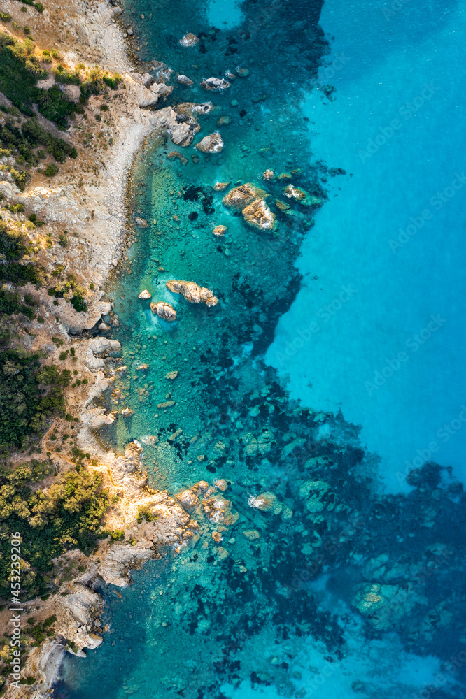 View from above, stunning aerial view of a green and rocky coastline bathed by a turquoise, crystal clear water. Costa Smeralda, Sardinia, Italy.