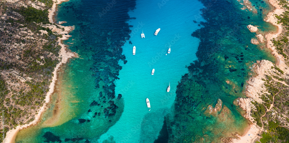 View from above, stunning aerial view of a green and rocky coastline bathed by a turquoise, crystal clear water. Costa Smeralda, Sardinia, Italy.
