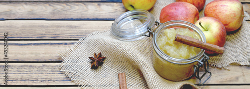 Photos homemade apple sauce in a glass jar with red apples and stick of cinnamon on a
