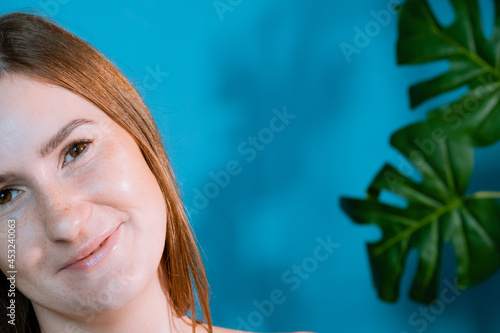 Pretty smiling joyfully female with brown hair, looking with satisfaction at camera, being happy. Studio shot of good-looking beautiful woman on background studio wall and tropical leafs.