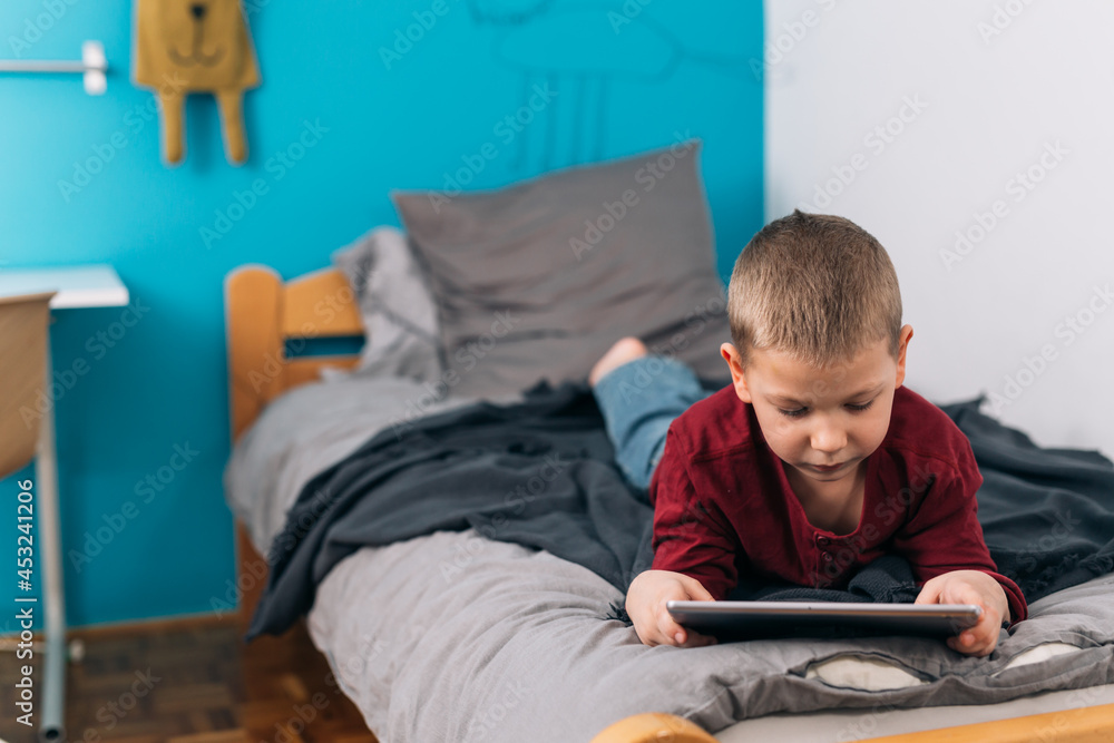 little boy laying on bed and using digital tablet
