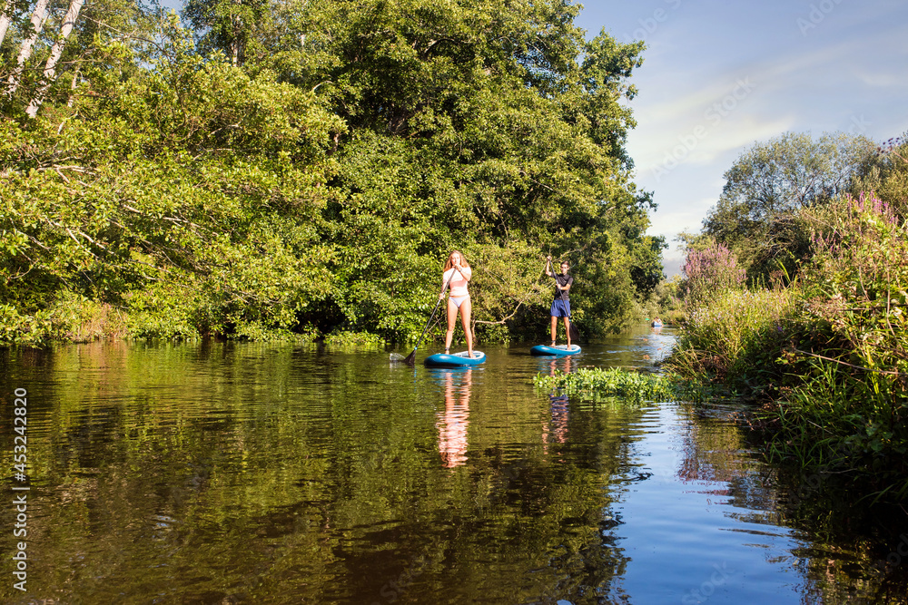 cute young couple paddle boarding on a river cute young couple paddle boarding on a river