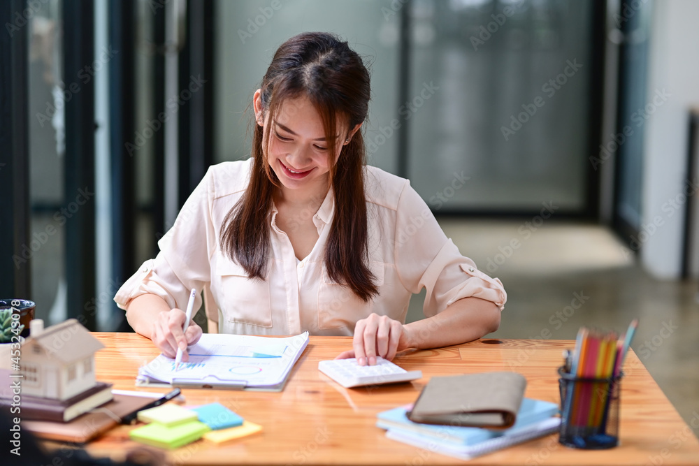 Asian female accountant checking financial documents and using calculator at her workplace. Asian female accountant checking financial documents and using calculator at her workplace.
