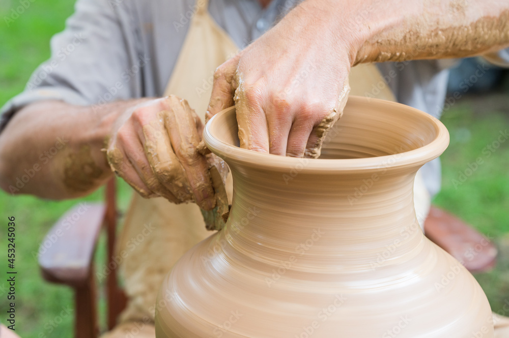Hands of a man making a clay vase on a potter's wheel