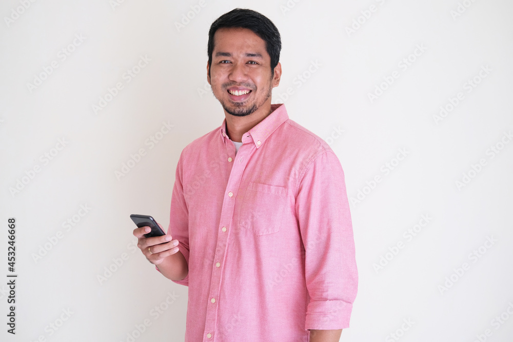 Attractive Asian man wearing pink shirt smiling confident while holding his smartphone Attractive Asian man wearing pink shirt smiling confident while holding his smartphone