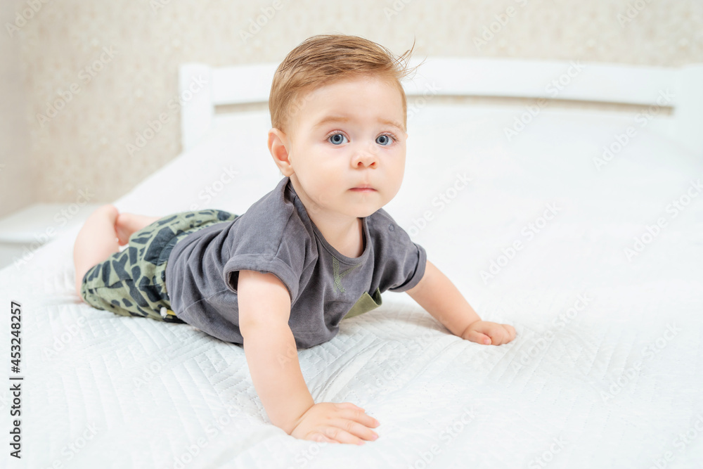 Beautiful baby lying on tummy in parent's bed. Adorable kid crawling on bed in white sunny bedroom. Beautiful baby lying on tummy in parent's bed. Adorable kid crawling on bed in white sunny bedroom.