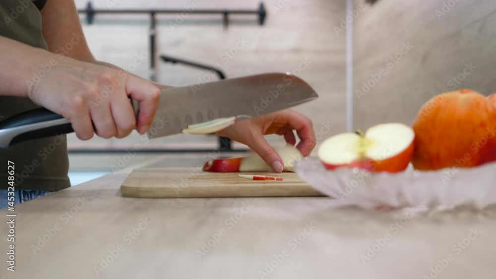 Happy woman is preparing the proper meal in the kitchen. Close-up of women's hands side view. A woman cuts an apple on a wooden kitchen board. Healthy food at home. Happy woman is preparing the proper meal in the kitchen. Close-up of women's hands side view. A woman cuts an apple on a wooden kitchen board. Healthy food at home.