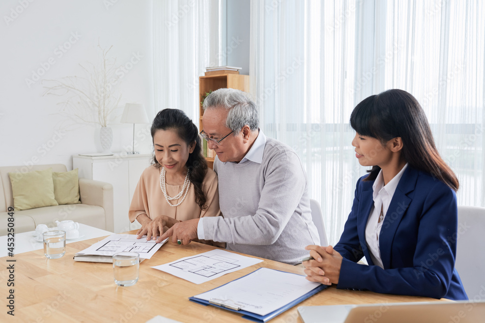 Smiling senior man and woman meeting with real estate broker and looking and building plans when choosing new house Smiling senior man and woman meeting with real estate broker and looking and building plans when choosing new house