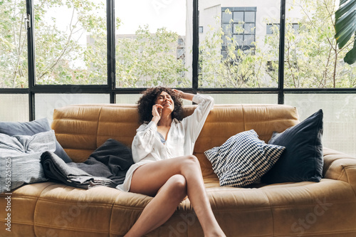 Young African American woman relaxing on couch talking on cellphone in a bright loft living room