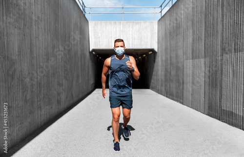 fitness  sport and health concept - young man in medical mask running outdoors