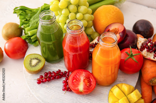 Bottles with healthy juice, fruits and vegetables on light background