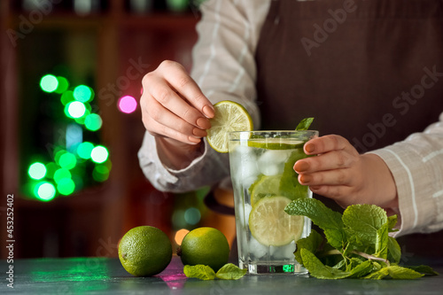 Female bartender making fresh mojito on table in bar