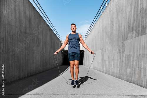 fitness, sport and exercising concept - man skipping with jump rope outdoors