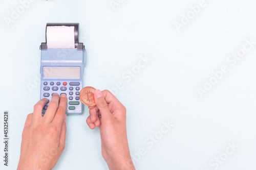 Payment for purchases with electronic money, bitcoin, e-commerce. Close-up of a hand holding a bitcoin coin and hand typing the amount, counting at the cash register. Business concept, online sale.