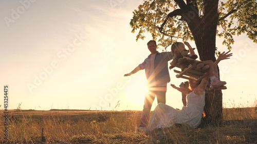 Happy little child with teddy rides on a swing with his parents at sunset in the park. Mom, daughter and dad are having fun at dawn. Happy family life concept. Kid with his beloved mother and father