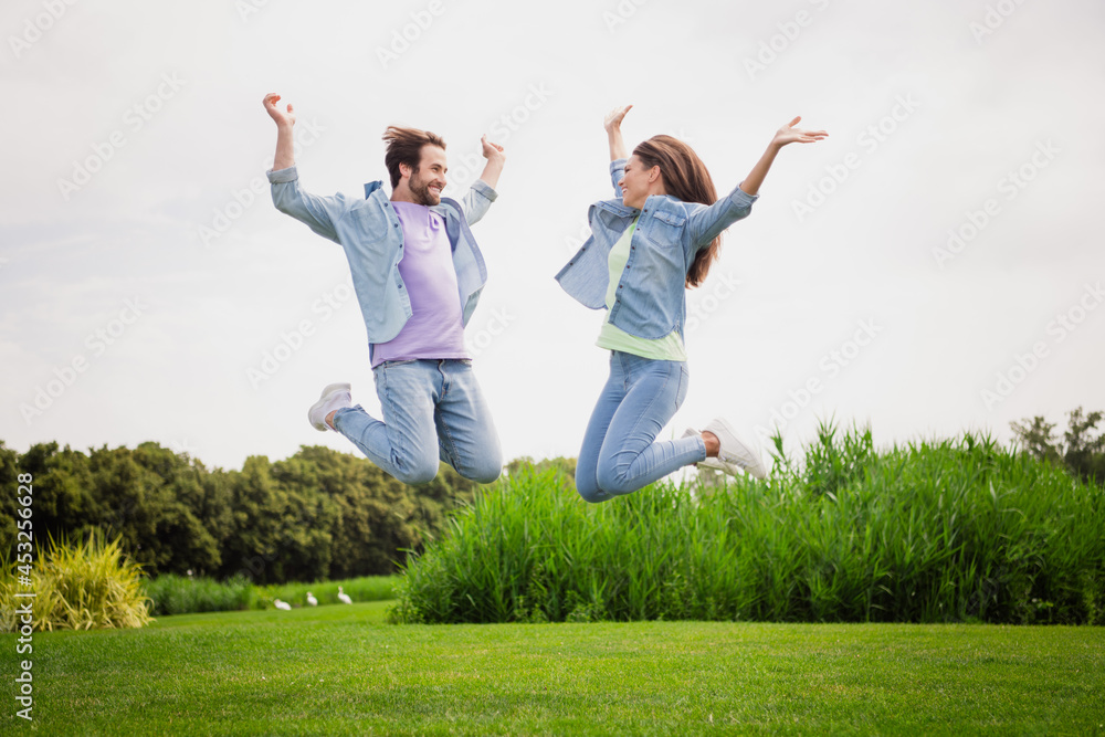Full size photo of smiling good mood married couple jumping raise hands in victory triumph enjoy summer holiday Full size photo of smiling good mood married couple jumping raise hands in victory triumph enjoy summer holiday