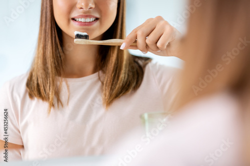 dental care  hygiene and people concept - happy smiling teenage girl with toothbrush brushing teeth at bathroom