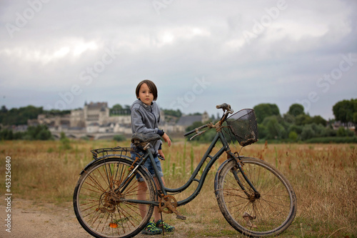 Beautiful preteen boy, child, standing next to an old bicycle in front of Amboise town in France