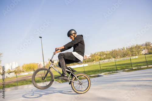 Crazy cyclist rides his low bike at the skatepark, bmx lifting the front wheel and being in the air twists his body, hips, performs tricks, laughs, smiles in the background trees, nature