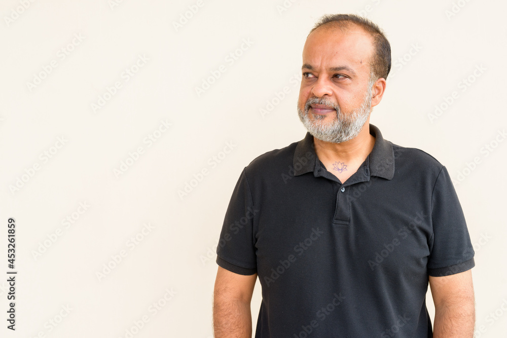 Fototapeta premium Portrait of handsome bearded Indian man thinking against plain wall