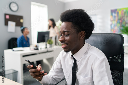 Portrait of handsome boss dressed in white shirt black tie pants dark skinned guy with afro manager sits at desk with computer in hand holds phone dials business numbers makes calls arranges meetings