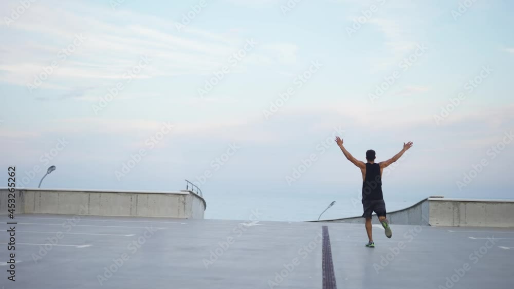 Man runs outdoors on the parking level garage with outstretched arms Man runs outdoors on the parking level garage with outstretched arms