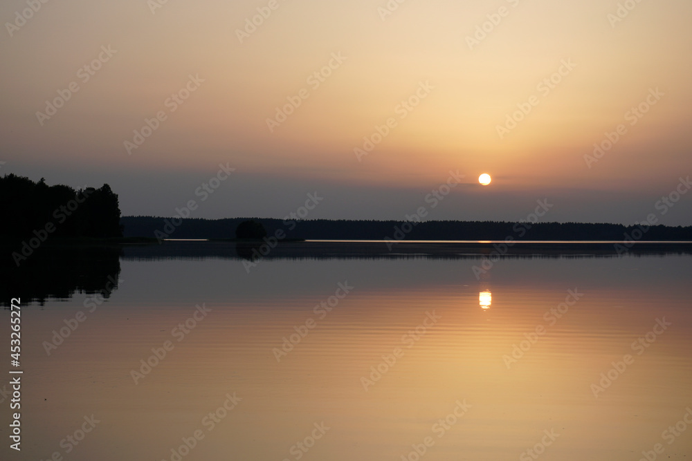 Quiet evening after a sultry day. Beautiful sunset over the lake. Reflection and horizon. Evening dim soft sun