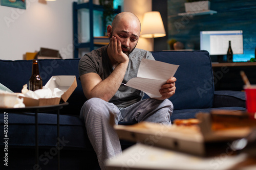 Desperate frustrated stressed young man reading letter, payment debt notification, bad financial report, eviction renter notice. Anxious, worried tenant by warning document for unpaid bank bills photo