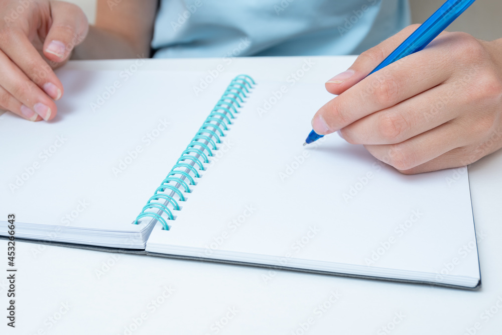Female student hand holding a pen writing in a notebook, large poan, copy space. Business woman makes a note in a notebook. Back to school concept. Business concept Female student hand holding a pen writing in a notebook, large poan, copy space. Business woman makes a note in a notebook. Back to school concept. Business concept